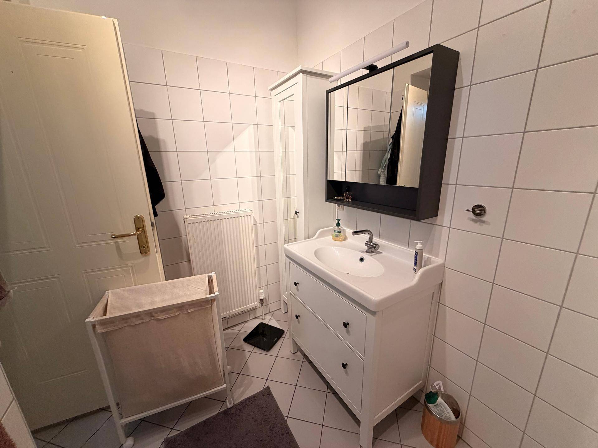 Badezimmer mit Waschbecken, Spiegelschrank und Heizkörper an der Wand.