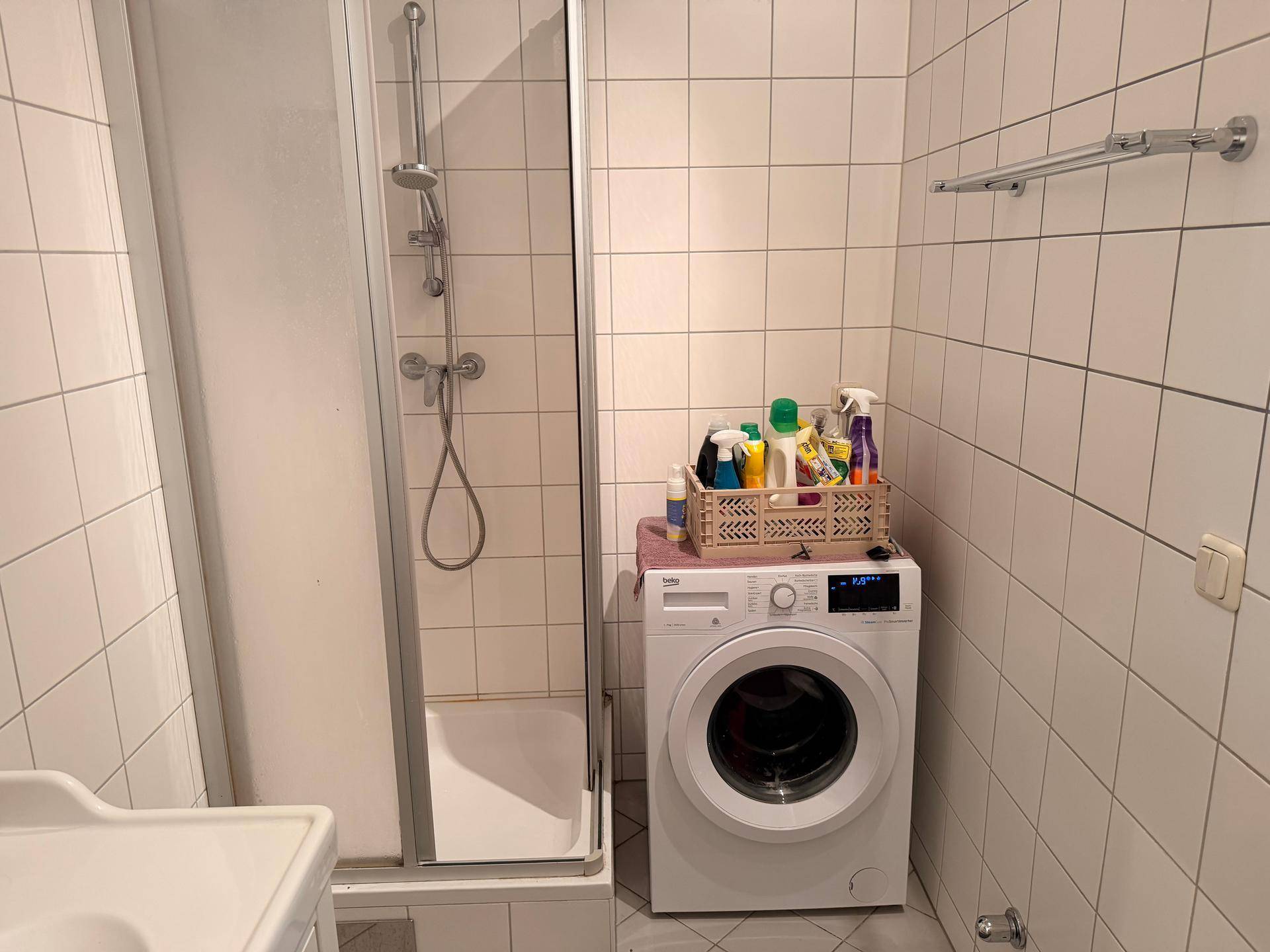 Badezimmer mit Duschkabine, Waschmaschine und weißen Wandfliesen.