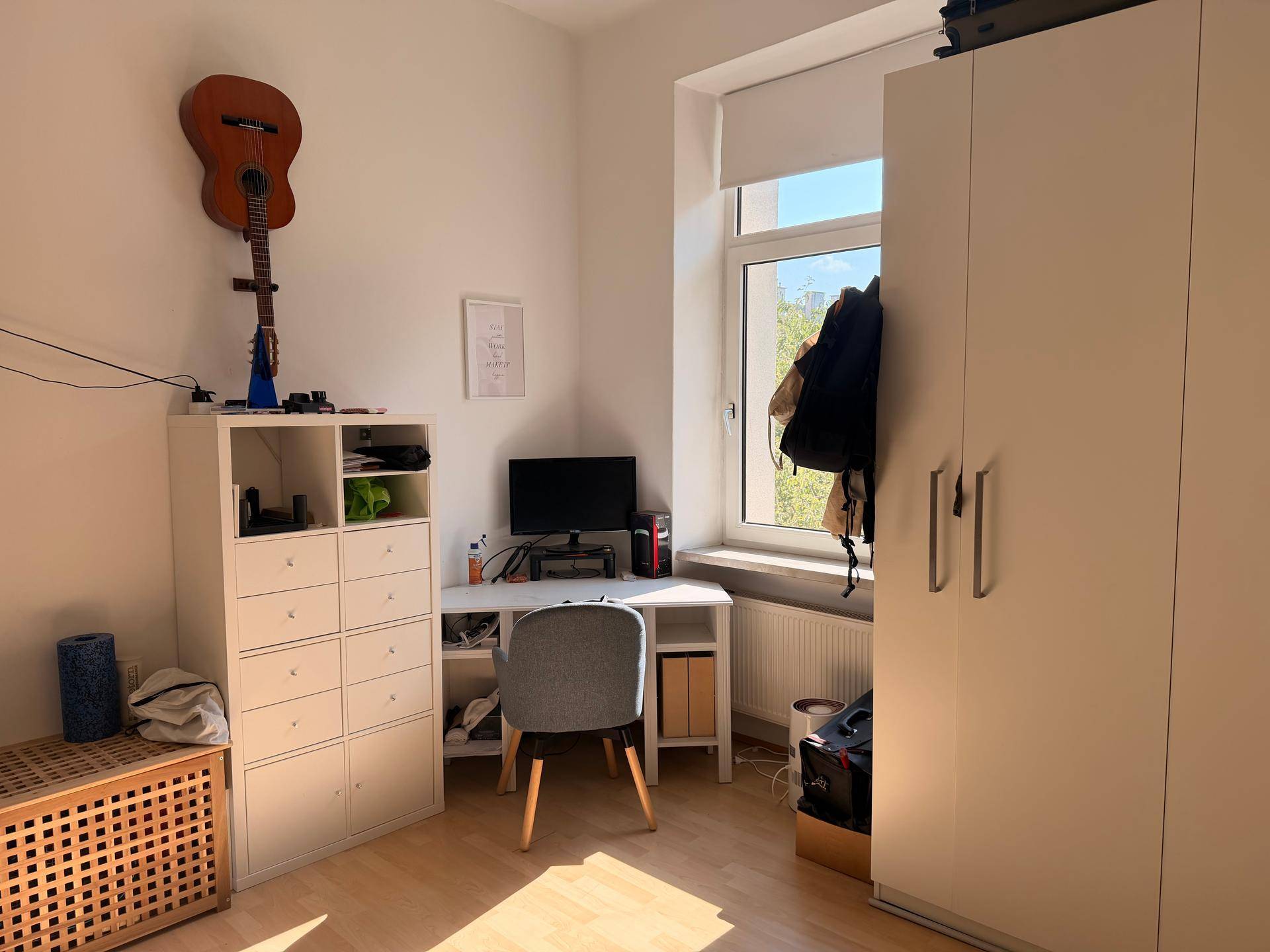 Schlafzimmer mit Schreibtisch, Kleiderschrank und großem Fenster für viel Tageslicht.