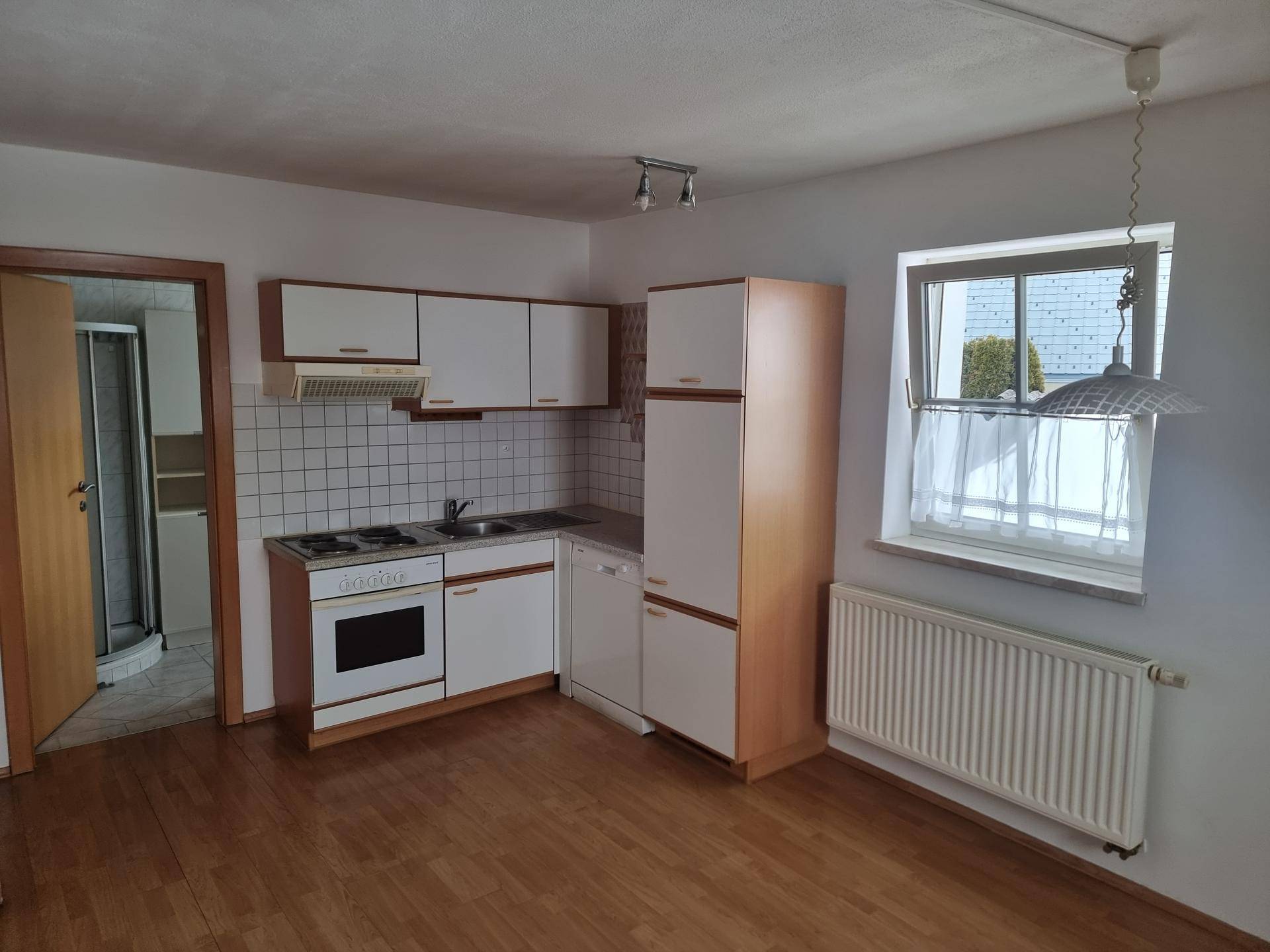 Funktionale Küche mit weißen Schränken, integrierten Geräten und Fensterblick.