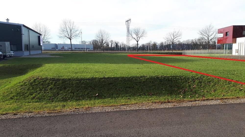 Grüne Rasenfläche eines Grundstücks mit angrenzenden modernen Gebäuden und einer roten Grenzmarkierung.