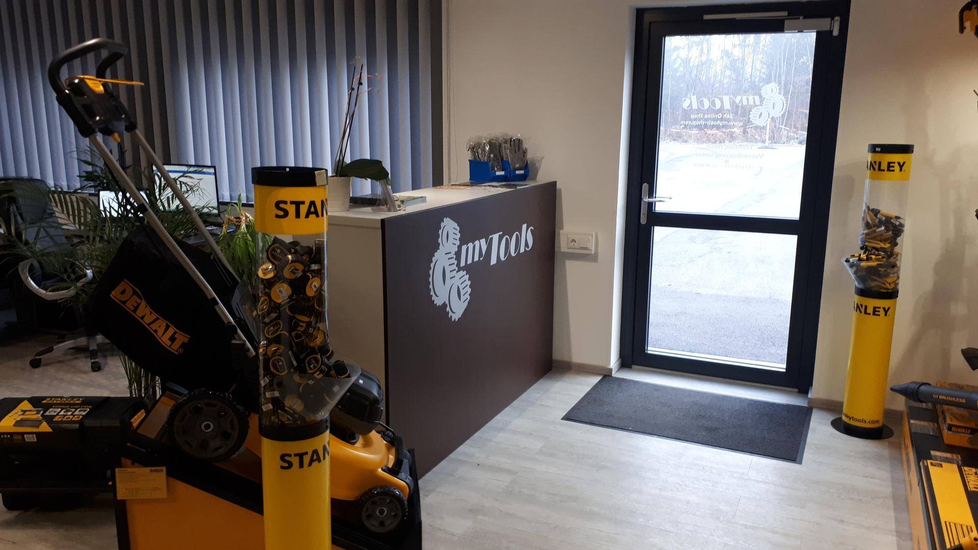 Empfangsbereich oder Showroom mit Theke, Glastür und Ausstellungsstücken, beleuchtet durch Tageslicht.