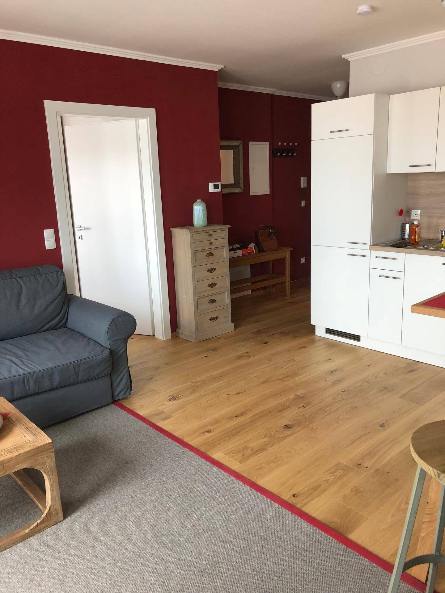 Offener Wohnbereich mit roter Wand, Sofa und Blick auf die Küchenzeile und den Flur.