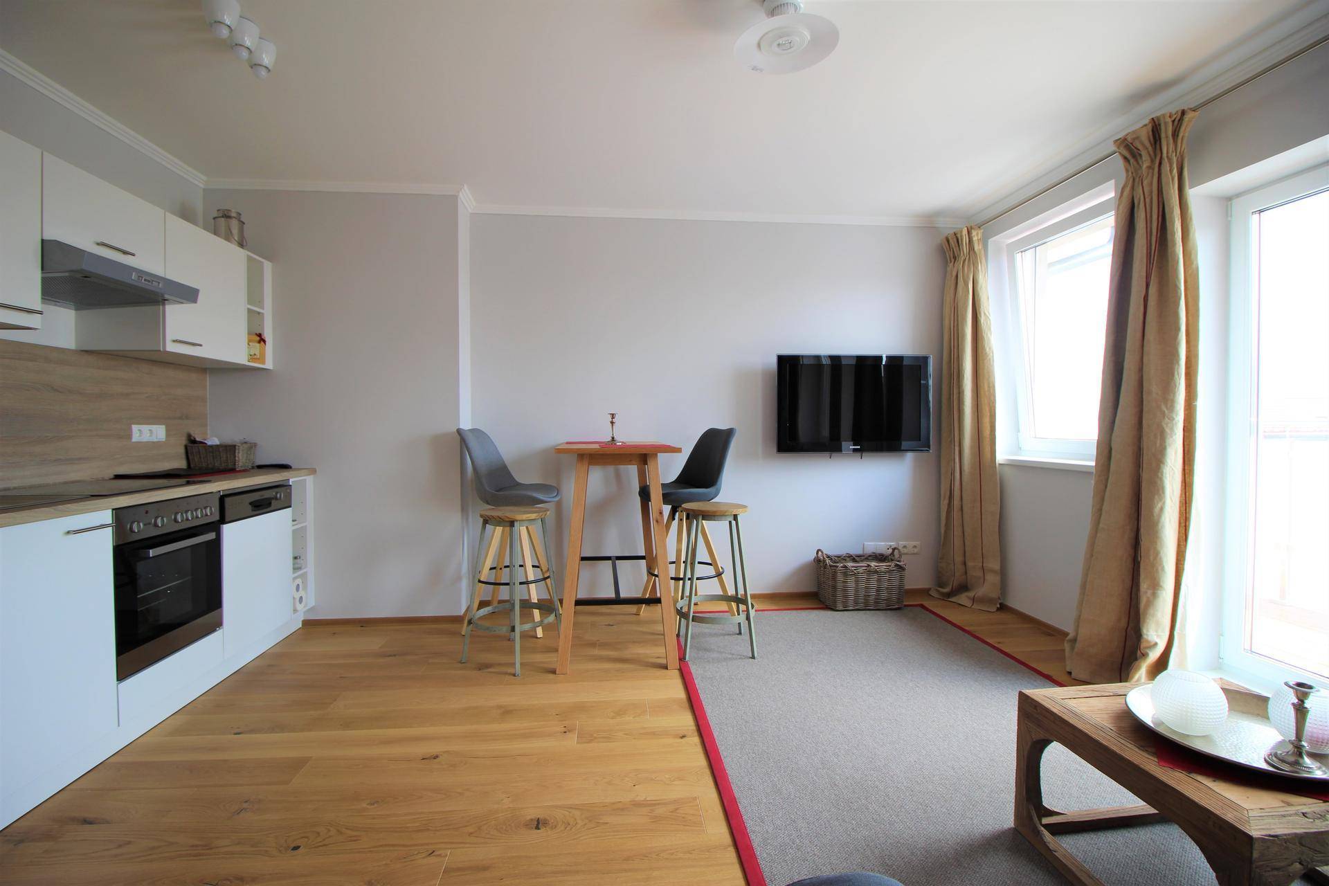 Offener Wohnbereich mit Küchenzeile, Essplatz und Fernseher an der Wand.