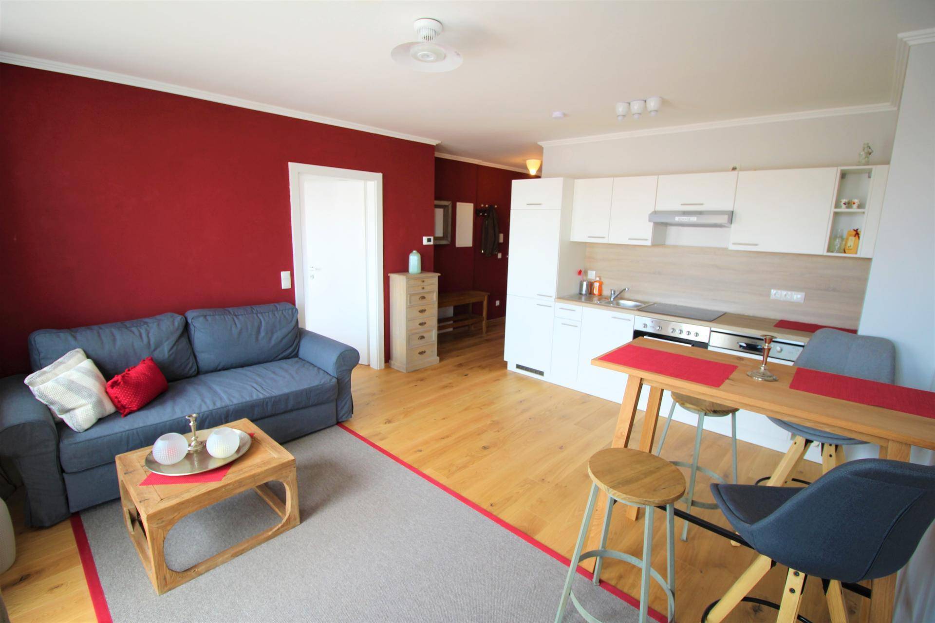 Gemütlicher Wohn-Essbereich mit roter Akzentwand, Sofa und integrierter Küchenzeile.
