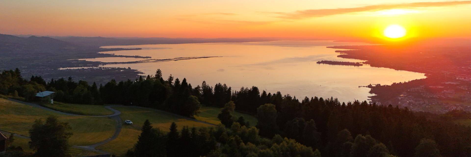 Atemberaubender Sonnenuntergang über einem weiten See, umgeben von bewaldeten Hügeln und einer weiten Landschaft.