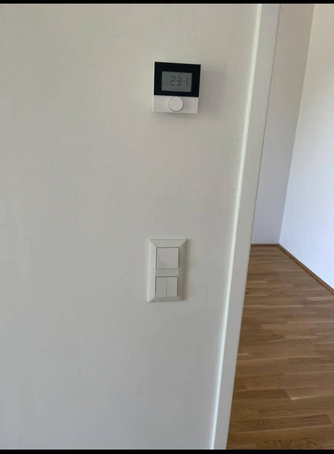 Thermostat und Lichtschalter an einer weißen Wand, die die Raumtemperatur regeln.