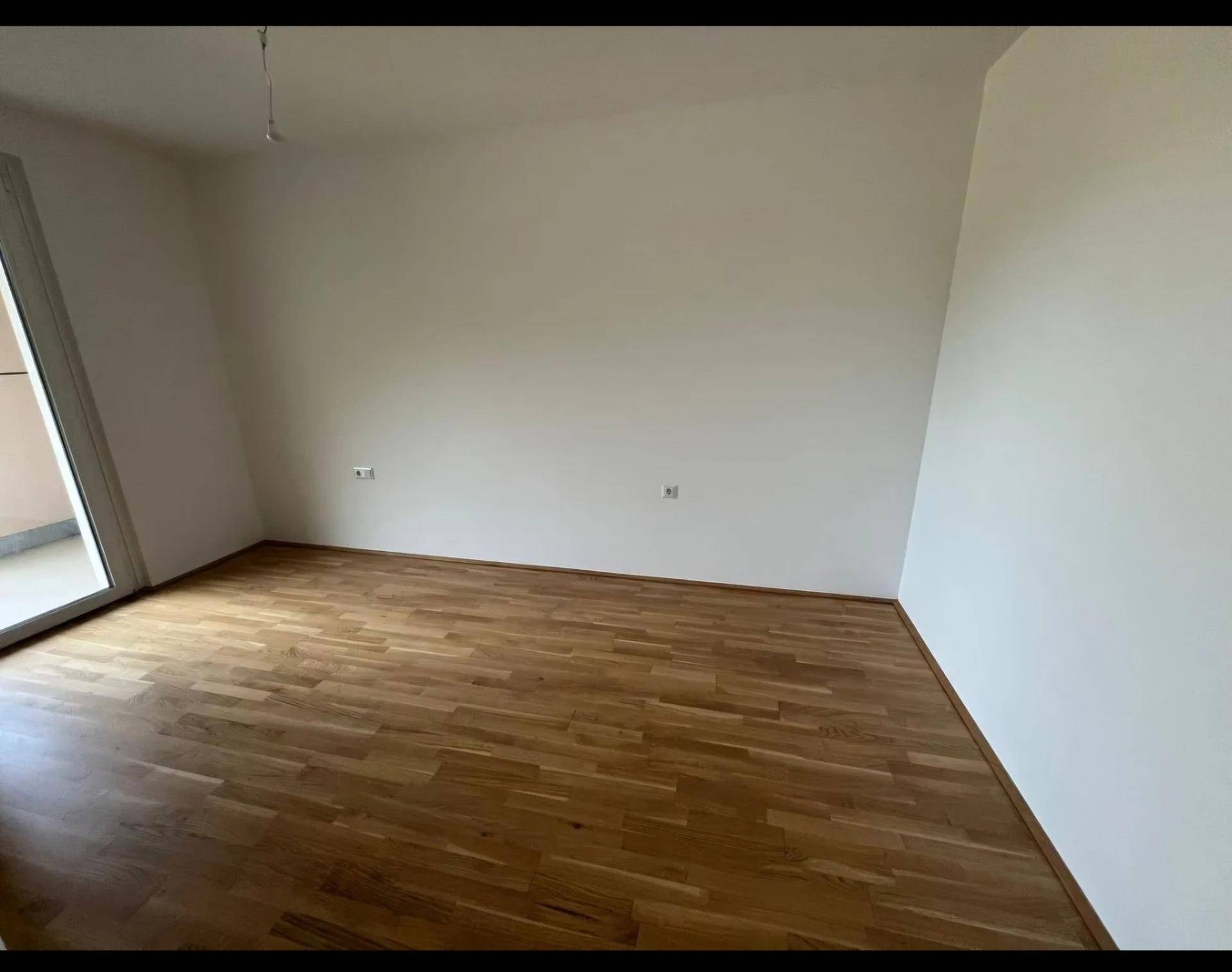 Leeres Zimmer mit Holzboden und weiß gestrichenen Wänden, bereit zur Einrichtung.