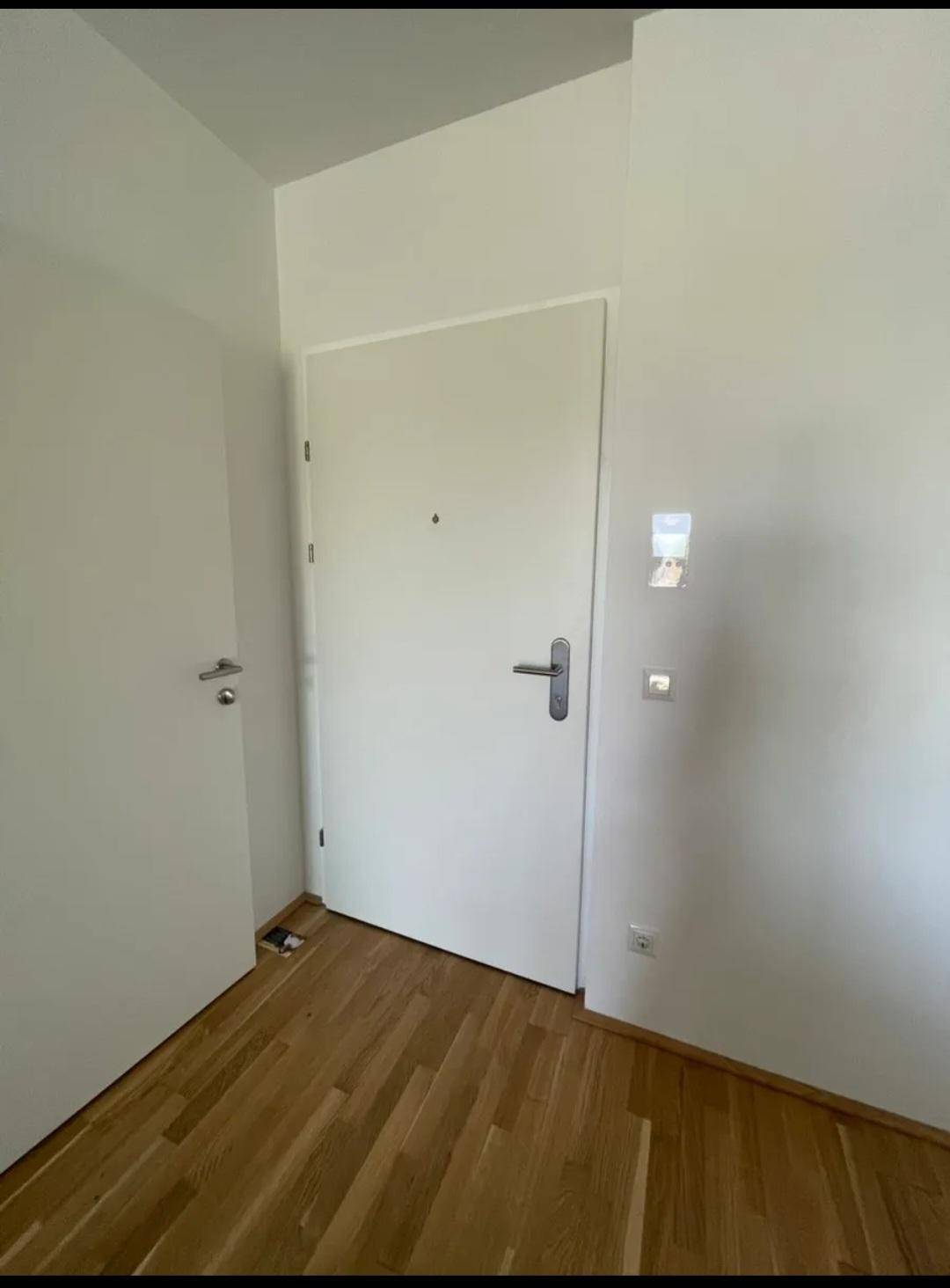 Eingangstür einer Wohnung mit Holzboden im Flur und moderner Gegensprechanlage.