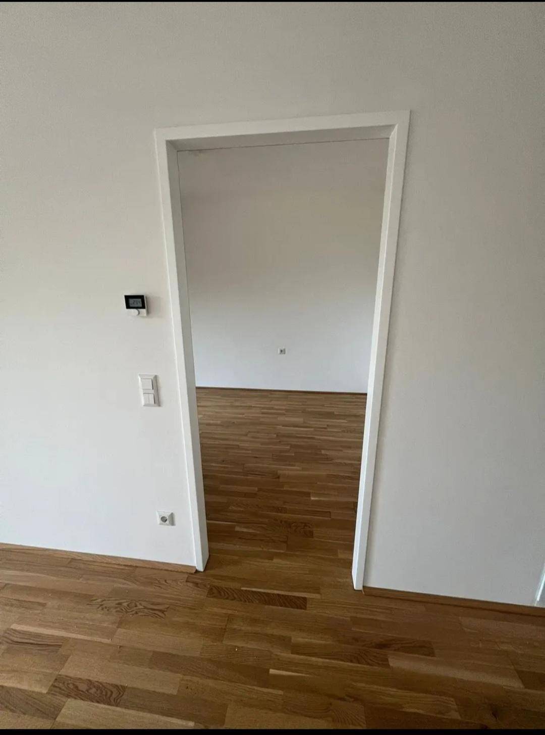 Heller Türrahmen verbindet zwei Räume mit durchgehendem Holzboden.