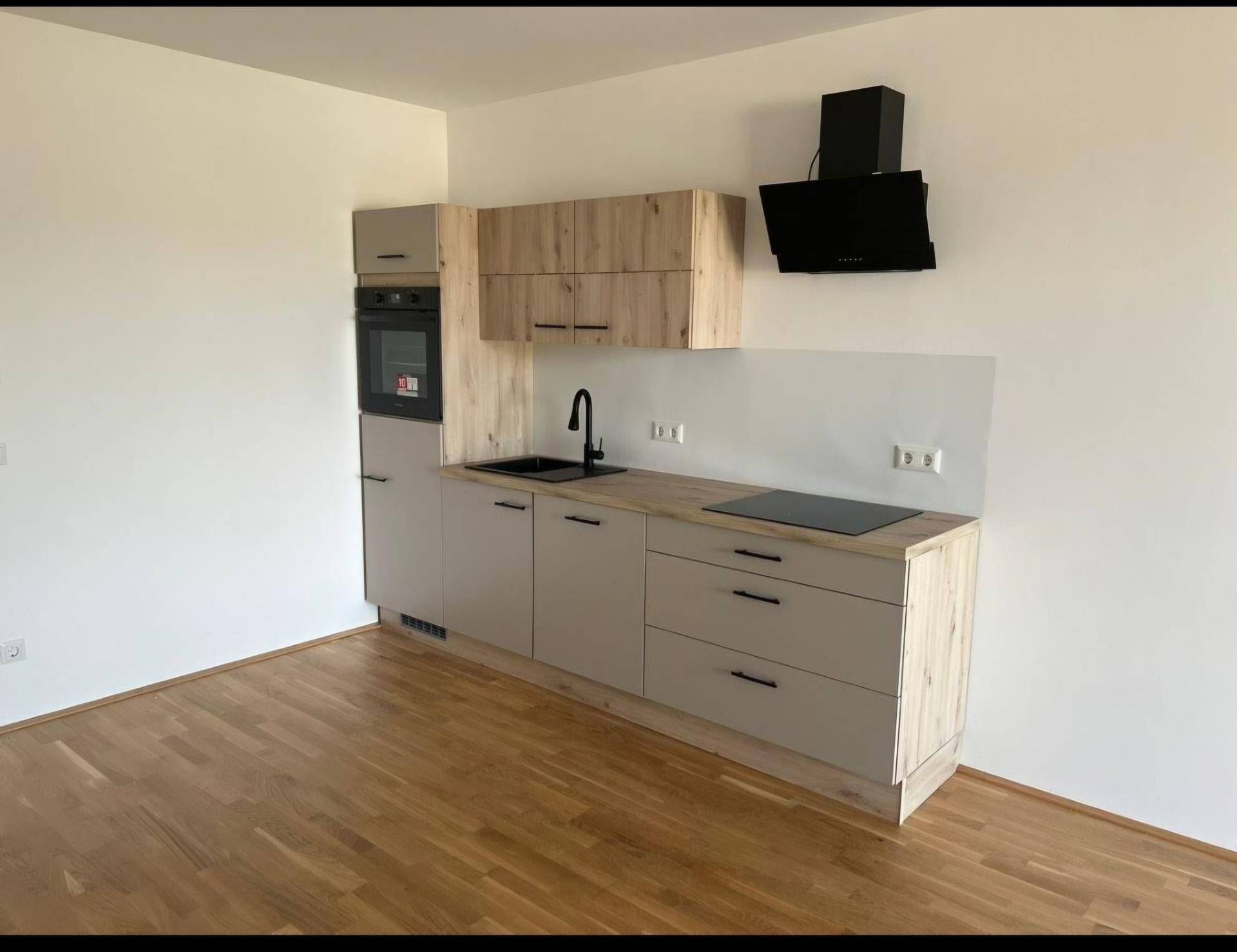 Moderne Einbauküche mit hellen Schränken, integrierten Geräten und dunkler Arbeitsplatte.