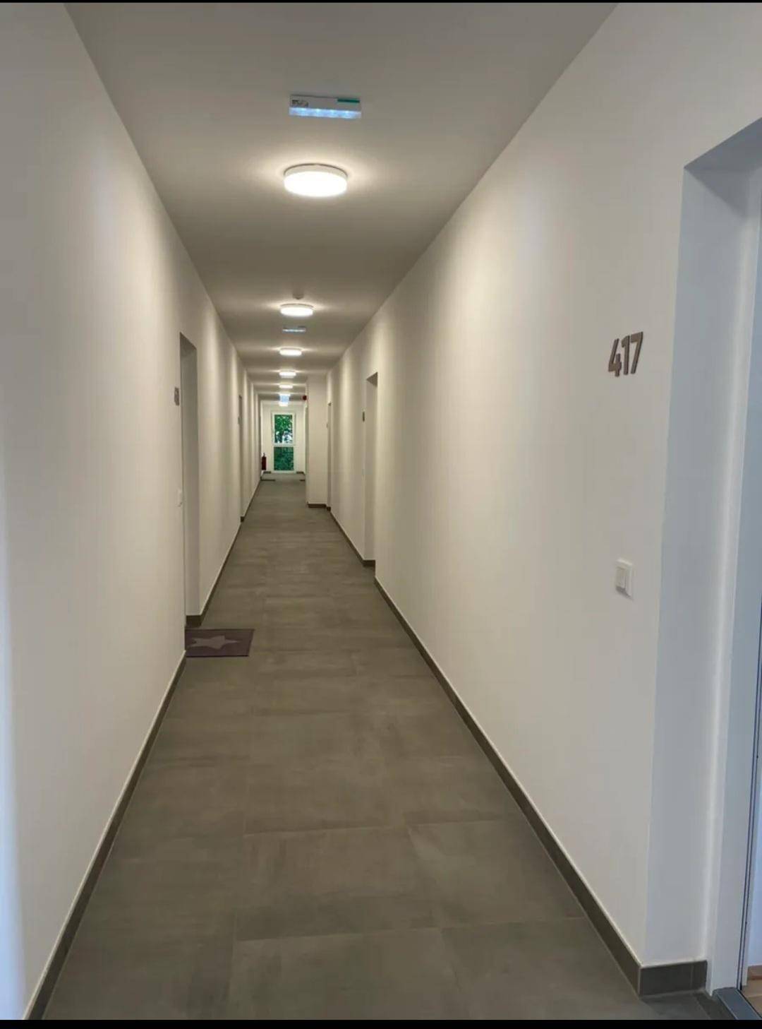Langer, heller Flur in einem Mehrfamilienhaus mit mehreren Wohnungseingängen.