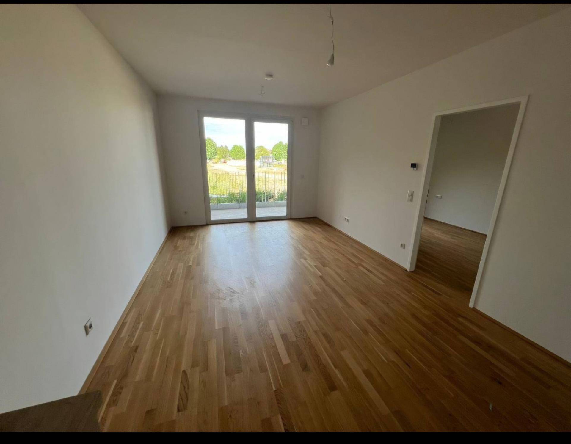 Geräumiges Wohnzimmer mit Holzboden und großen Fenstern, die viel Tageslicht hereinlassen.