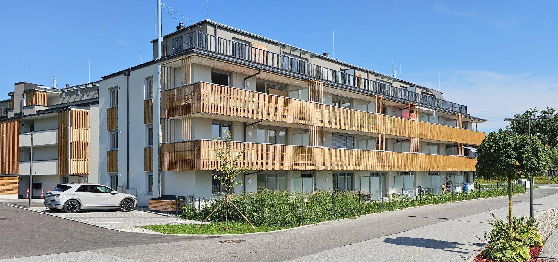 Ansicht des modernen Mehrfamilienhauses mit Holzfassadenelementen und einem geparkten Auto davor.