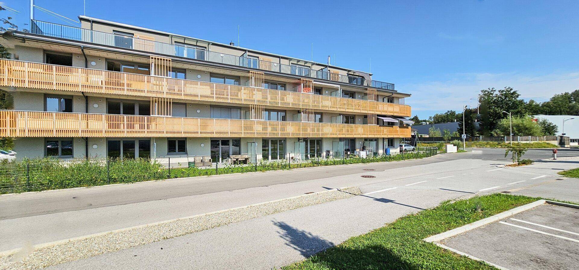 Moderne Wohnanlage mit mehreren Etagen und Balkonen mit Holzverkleidung unter blauem Himmel.