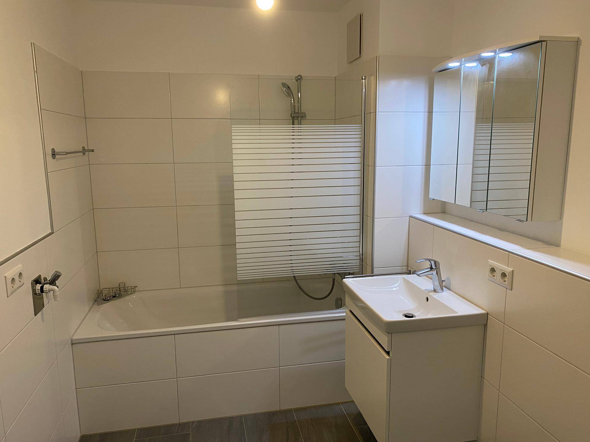 Funktionales Badezimmer mit Badewanne, Einzelwaschbecken und Spiegelschrank, komplett gefliest.