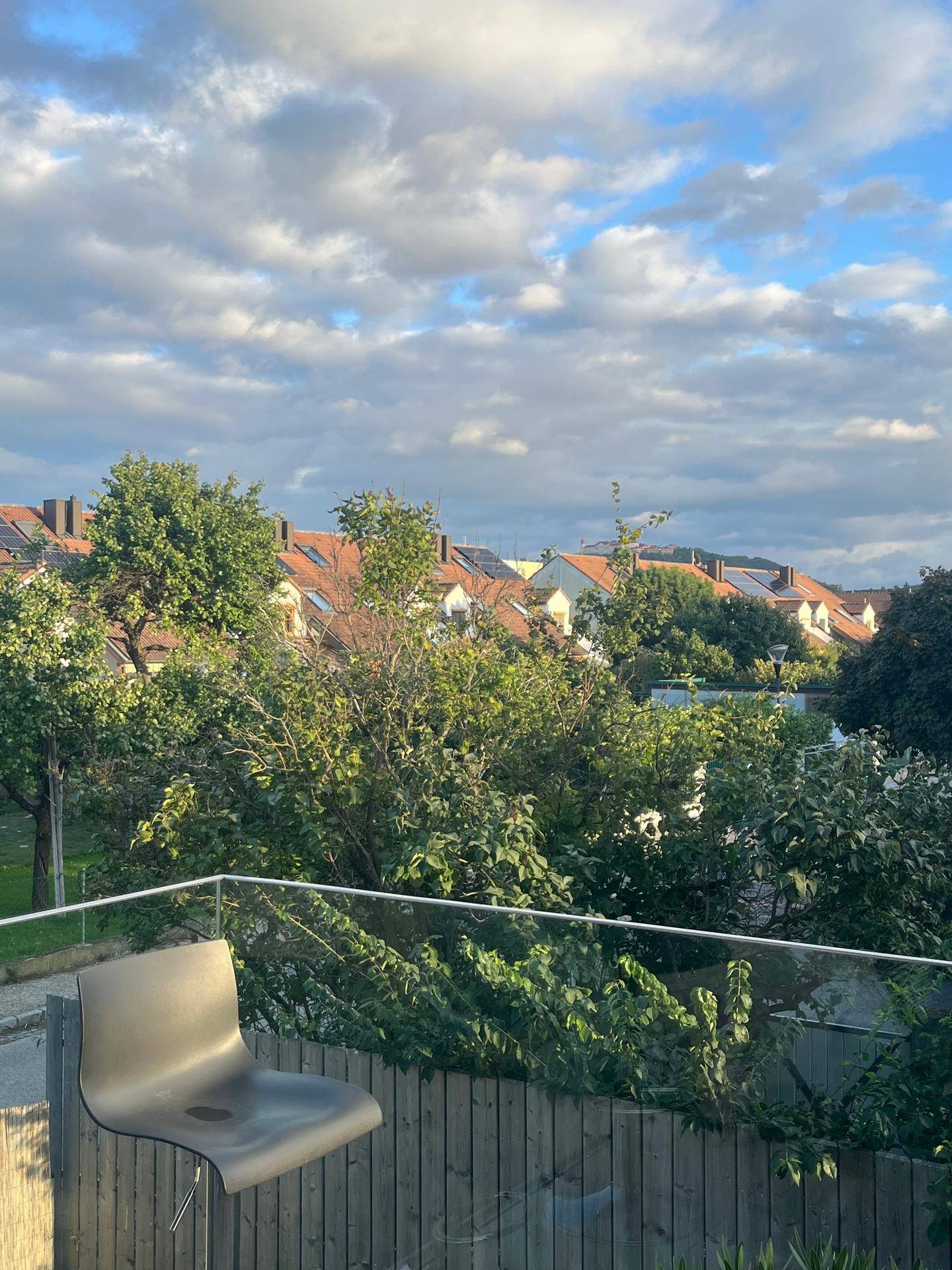 Balkon mit weitem Blick über die Nachbarschaft und grüne Baumwipfel, unter blauem Himmel.