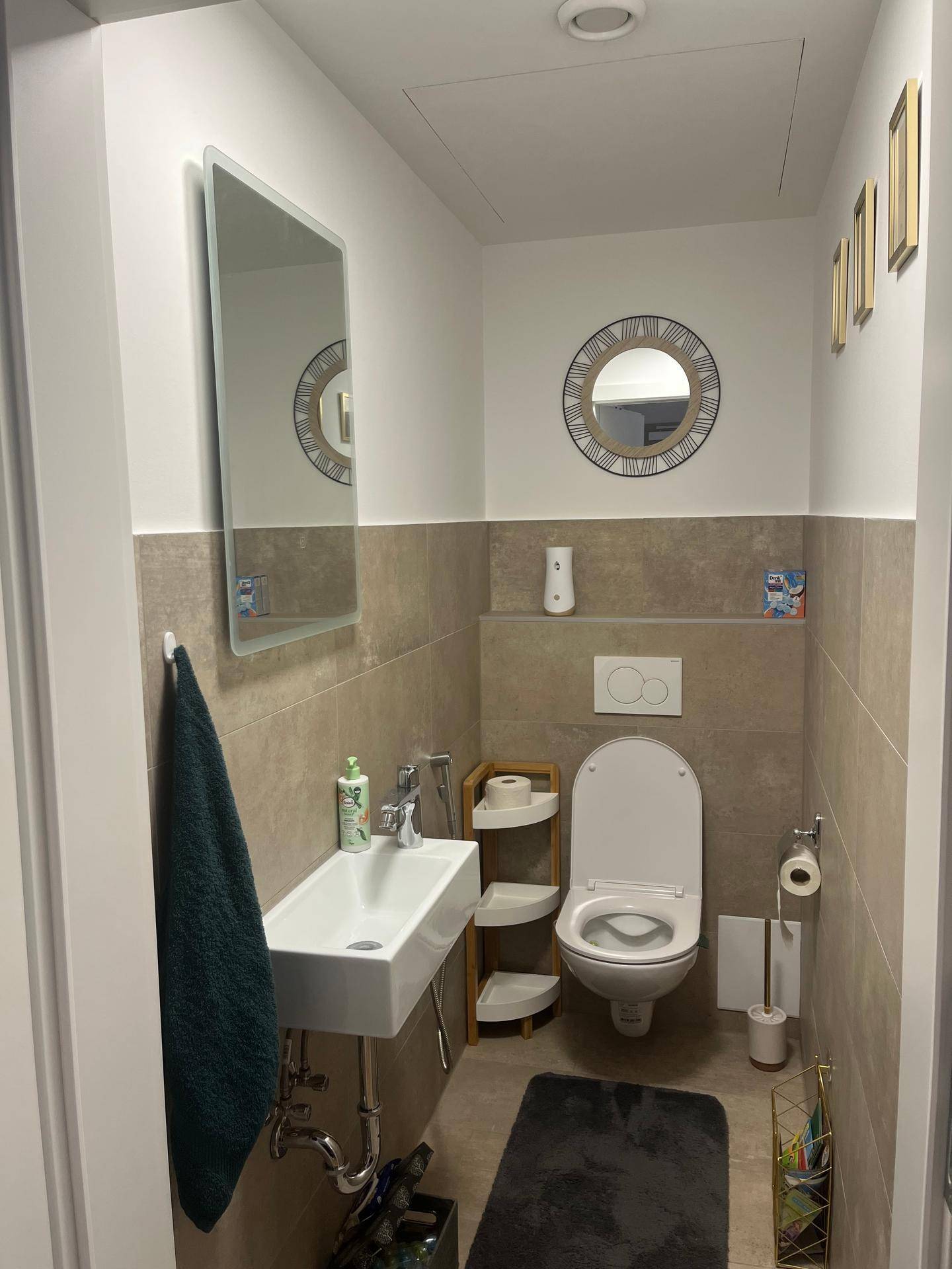 Modernes Gäste-WC mit Wand-WC, kleinem Waschbecken und beigen Fliesen, sauber und hell.