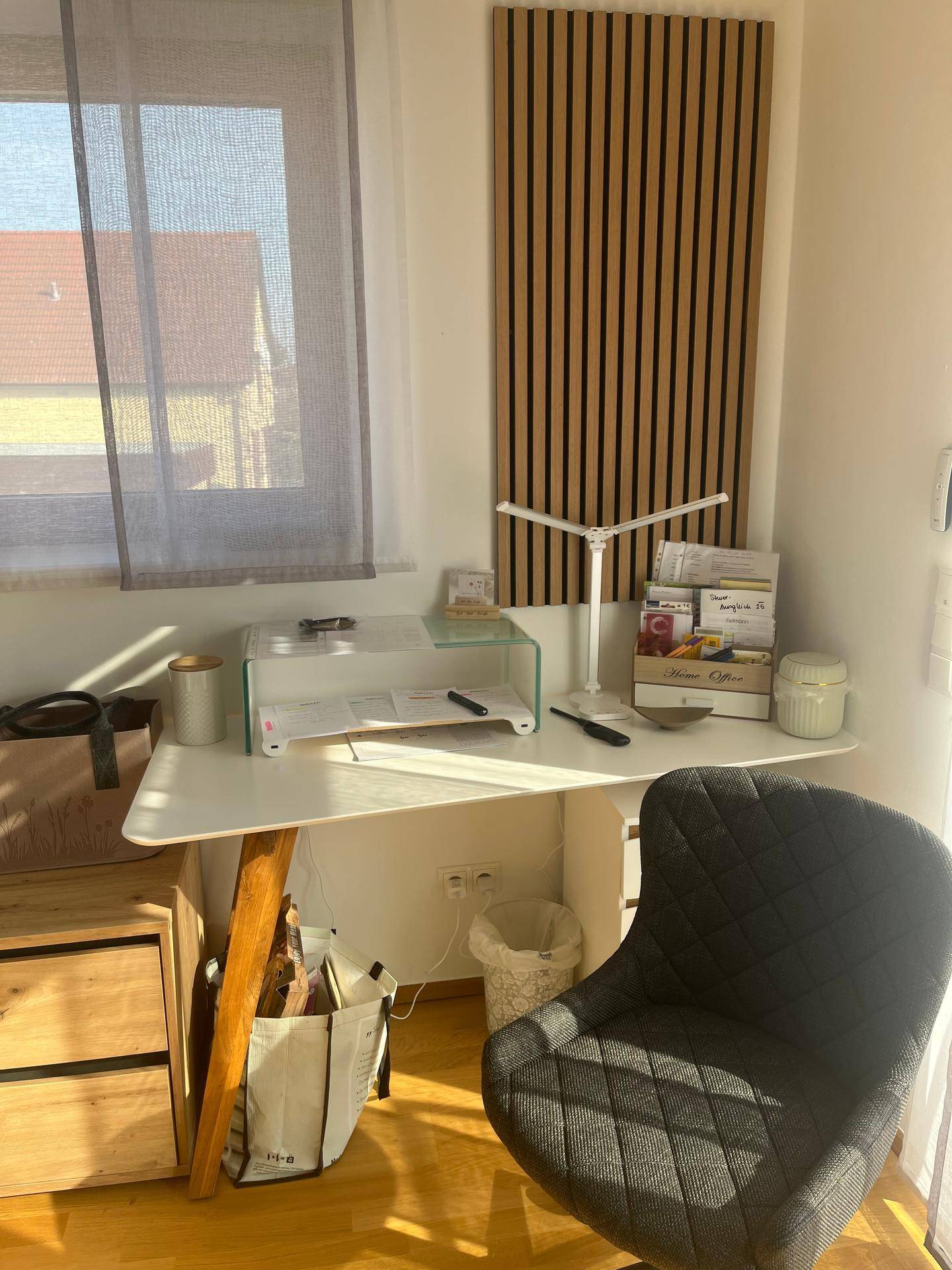 Heller Arbeitsbereich mit Schreibtisch, modernem Stuhl und Holzpaneel an der Wand, sonnendurchflutet.