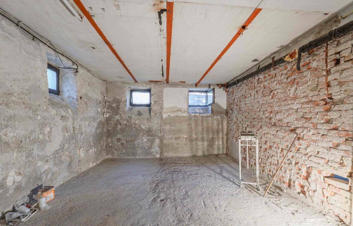 Kellerraum mit unverputzten Ziegelwänden und kleinen Fenstern, ideal für Lagerung oder Ausbau.