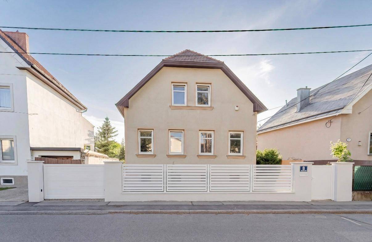 Renovierte Hausfassade mit Satteldach und modernem Zaun zur Straße hin.