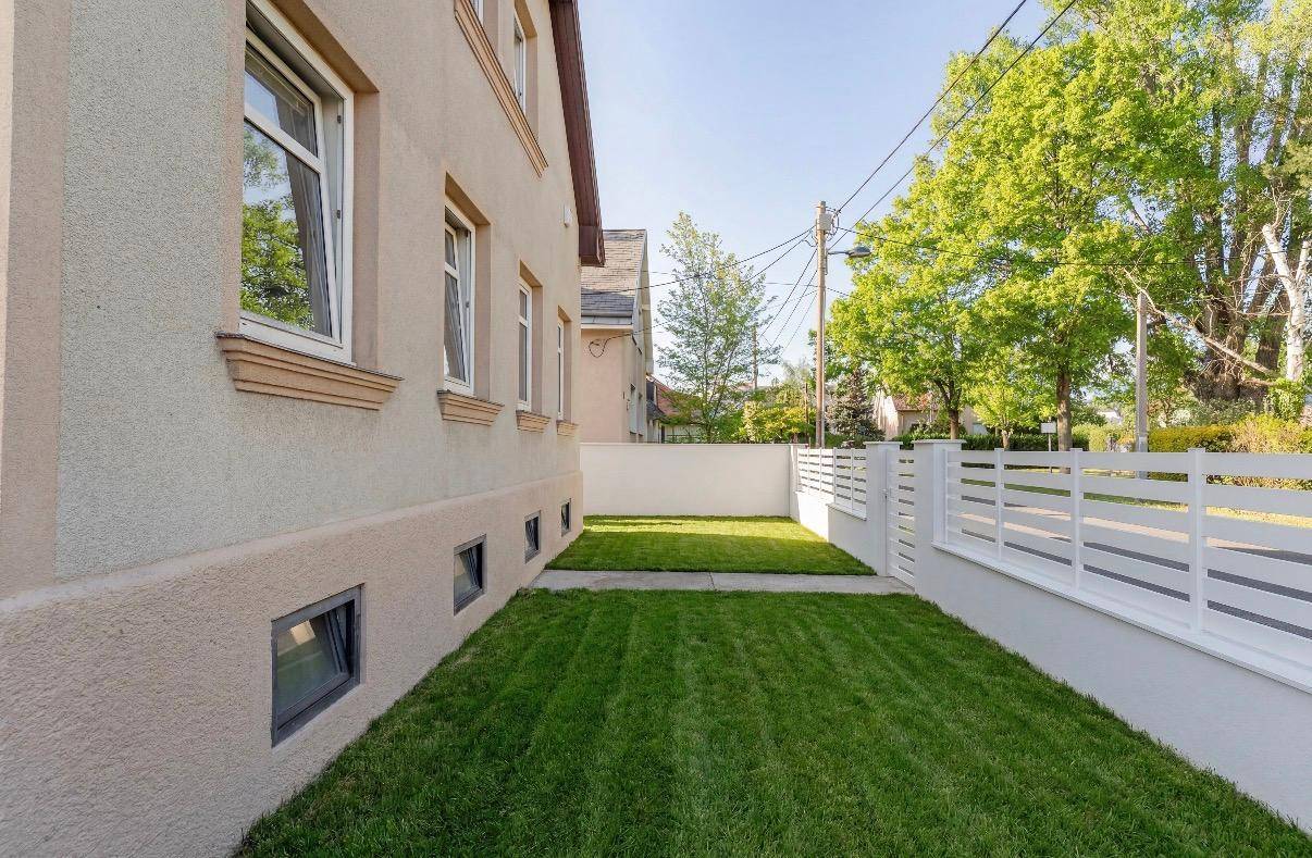 Seitlicher Gartenbereich mit gepflegtem Rasen und Zugang zum Haus, umgeben von einem Zaun.
