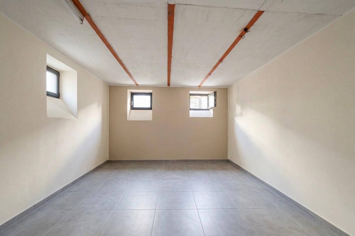 Renovierter Kellerraum mit grauen Fliesen und kleinen Fenstern, hell und funktional.
