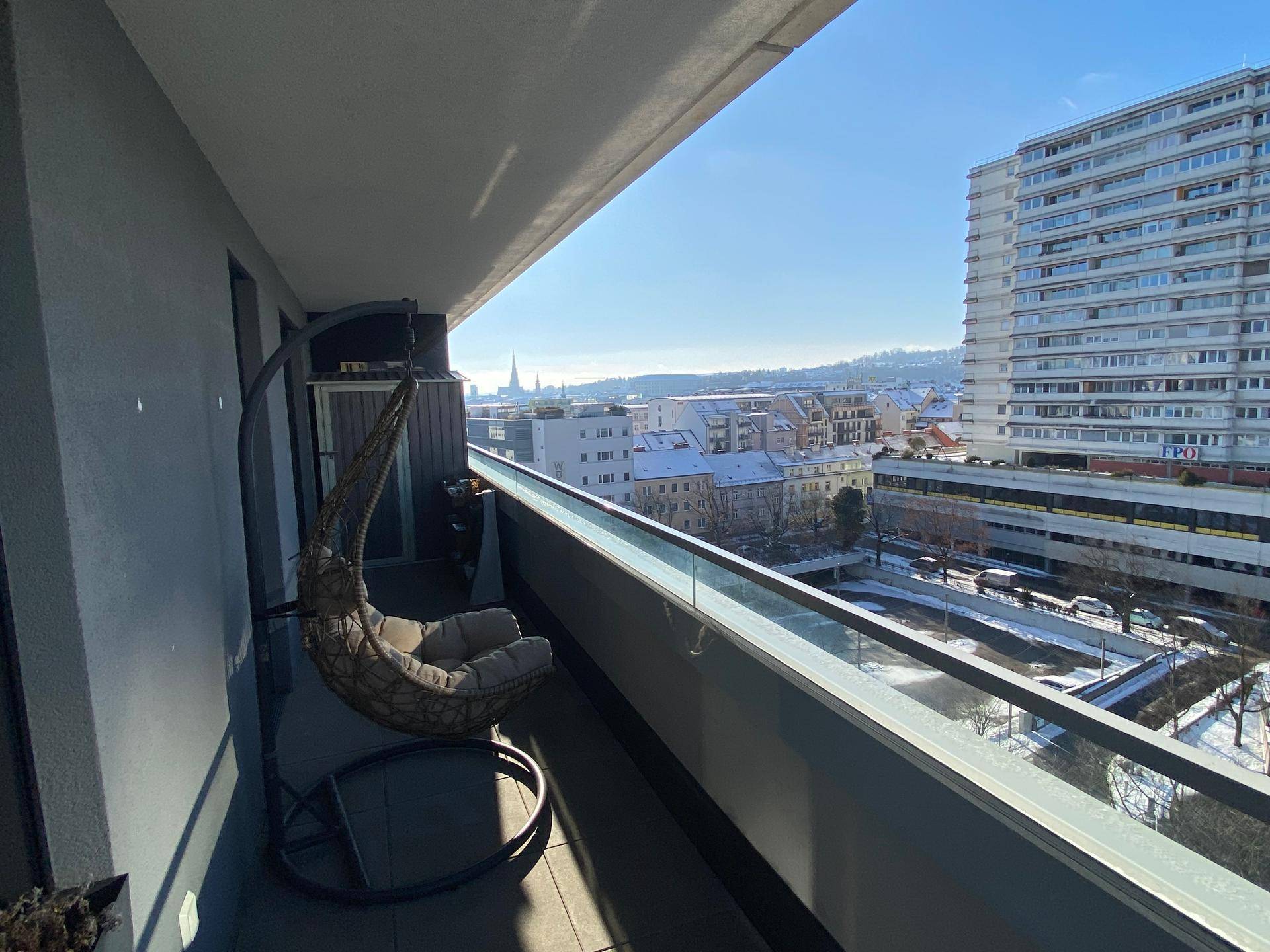 Möblierter Balkon mit Hängesessel und weitem Blick über die Stadtlandschaft.