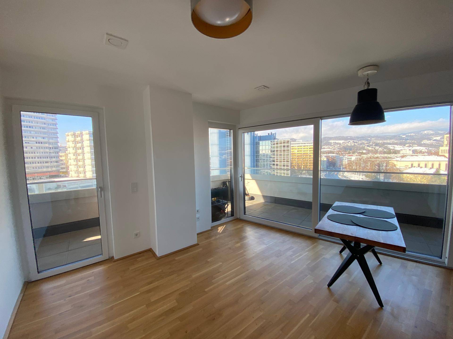 Heller Wohn-Essbereich mit Parkettboden und großen Fenstern mit Zugang zum Balkon.