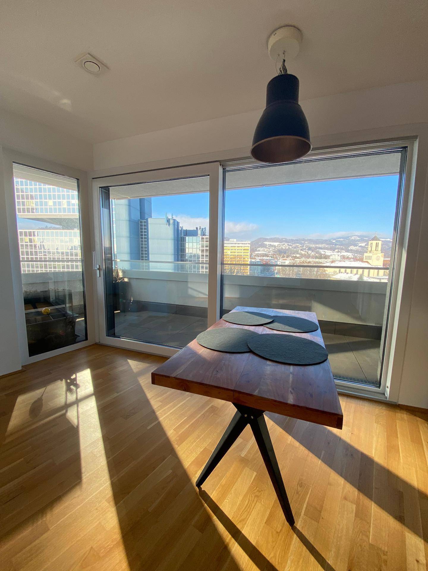 Lichtdurchfluteter Wohn-Essbereich mit Panoramablick auf die Stadt und die verschneiten Berge.