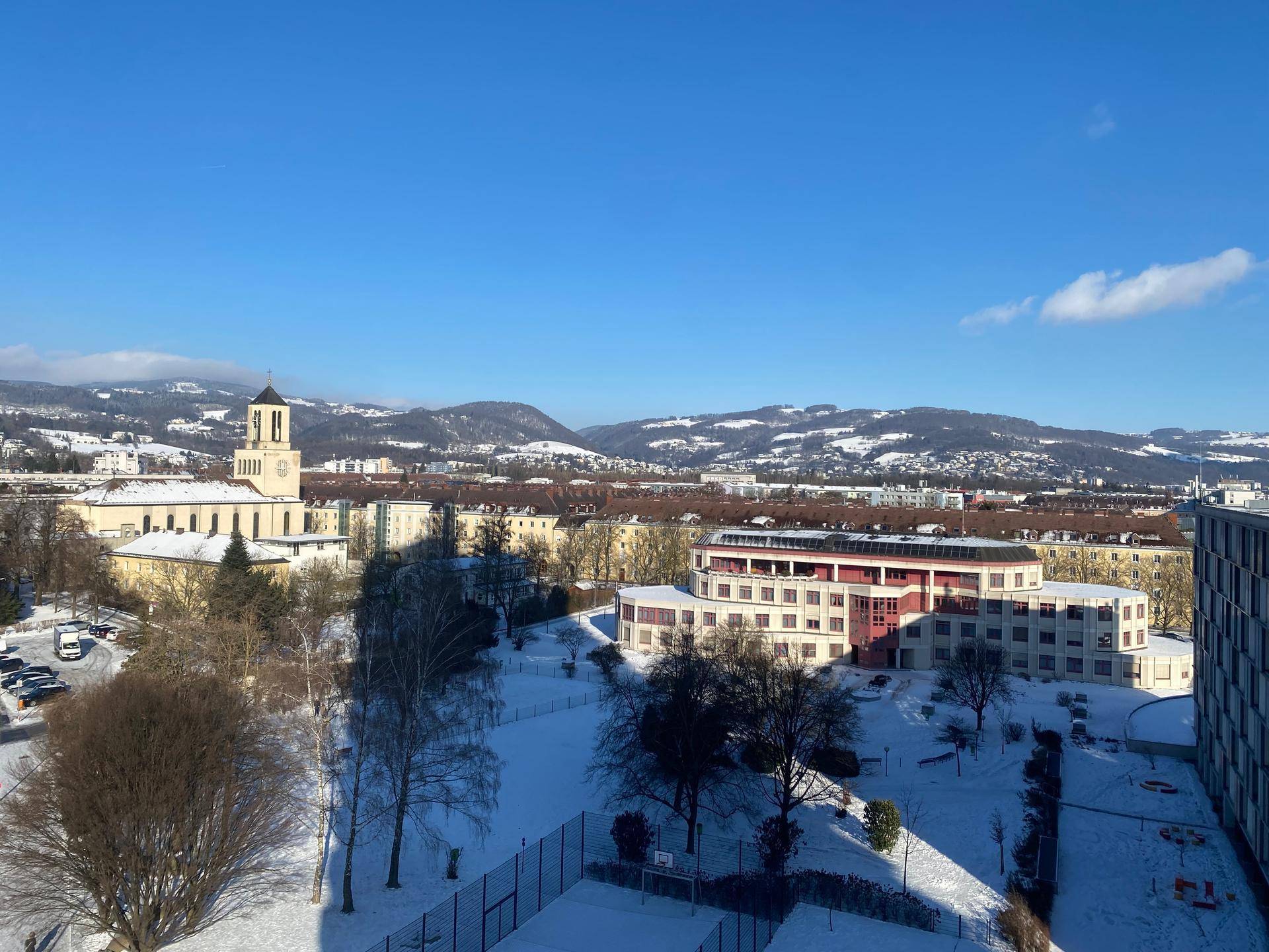 Panoramablick auf eine verschneite Stadtlandschaft mit Bergen unter blauem Himmel.