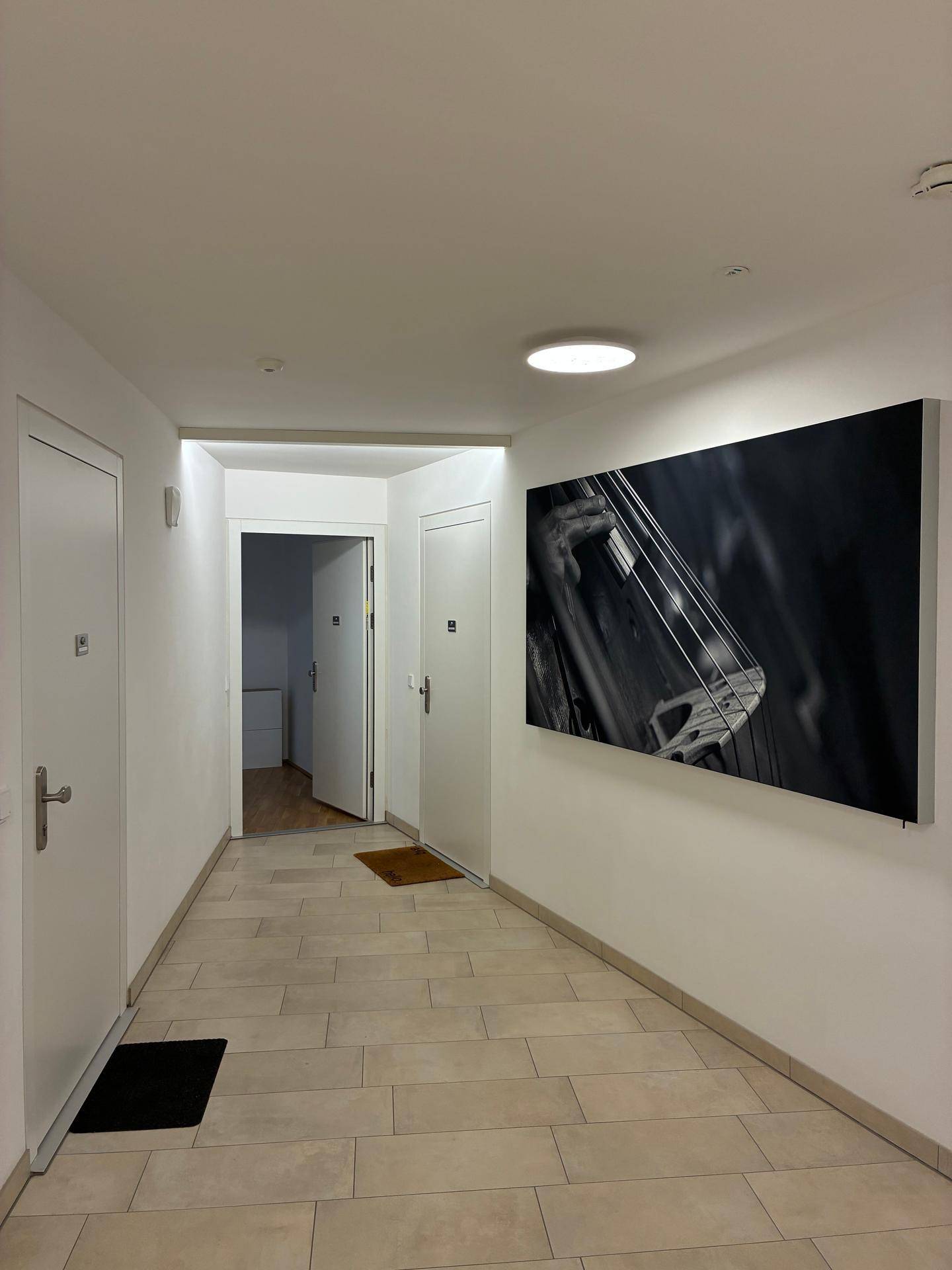 Heller Flur mit Fliesenboden und einem großen, modernen Kunstwerk an der Wand.