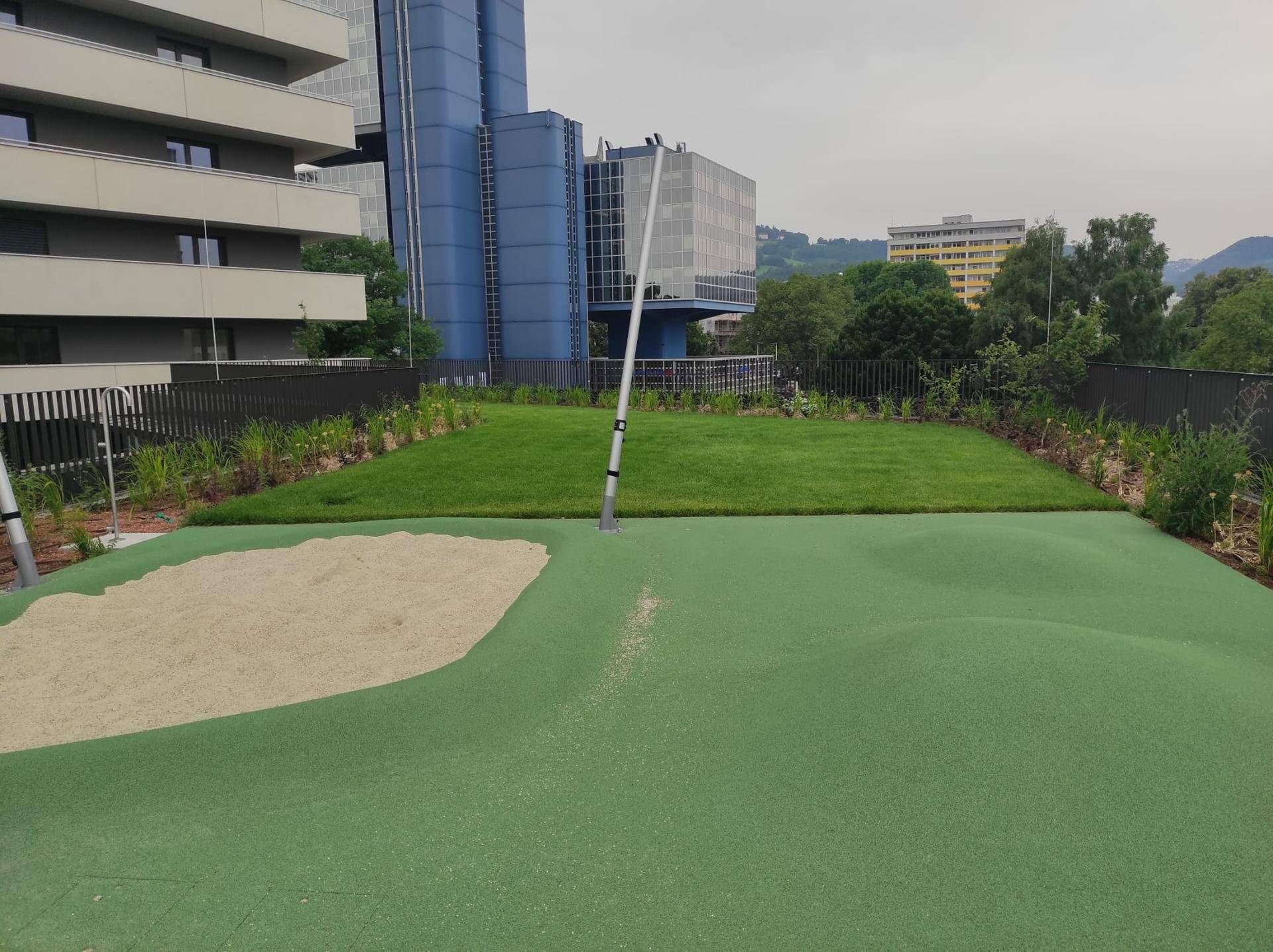 Dachgarten mit Rasenfläche, Sandbereich und Spielmöglichkeiten für Kinder.