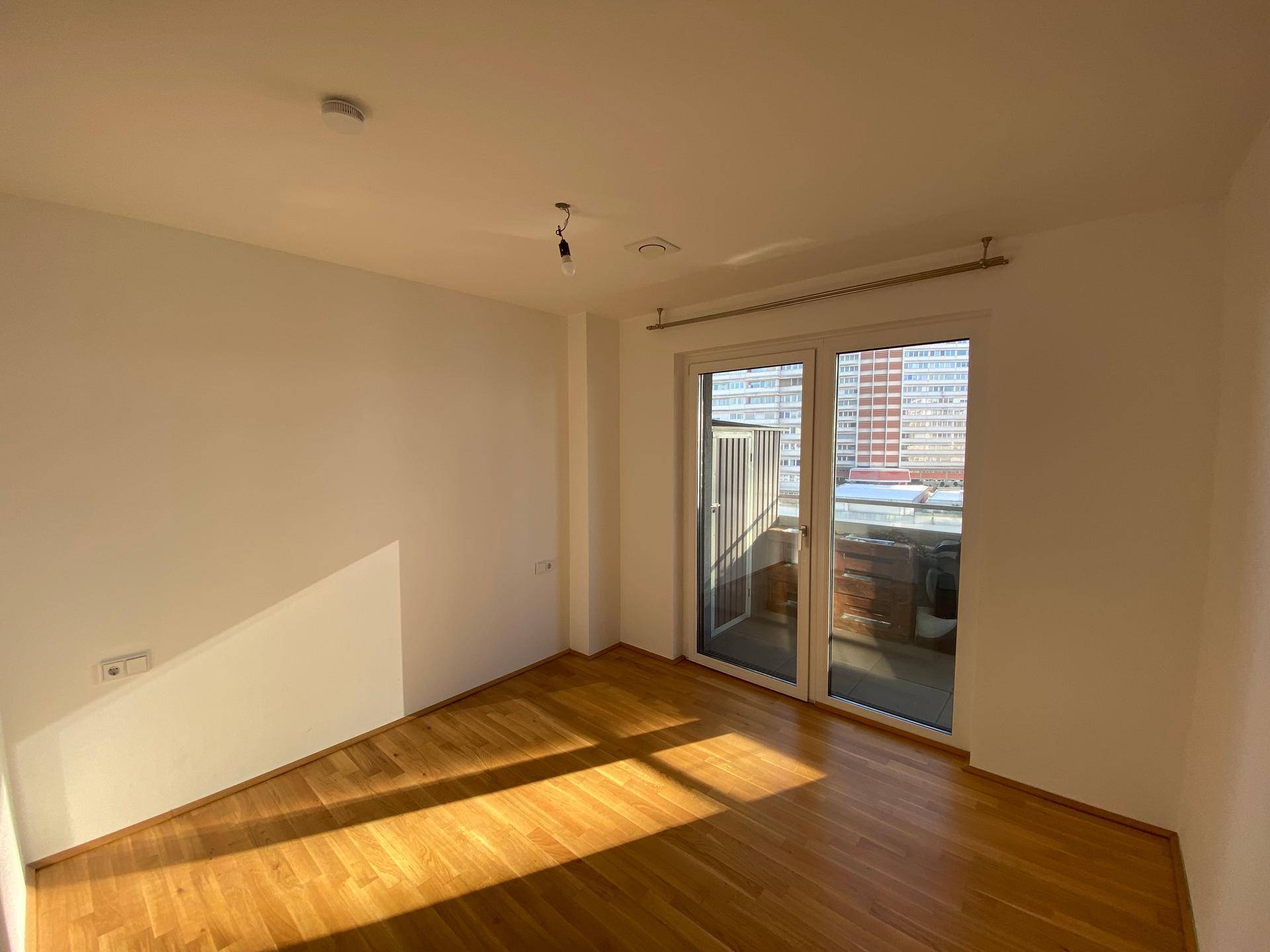 Heller Raum mit Parkettboden und direktem Zugang zu einem Balkon durch große Schiebetüren.