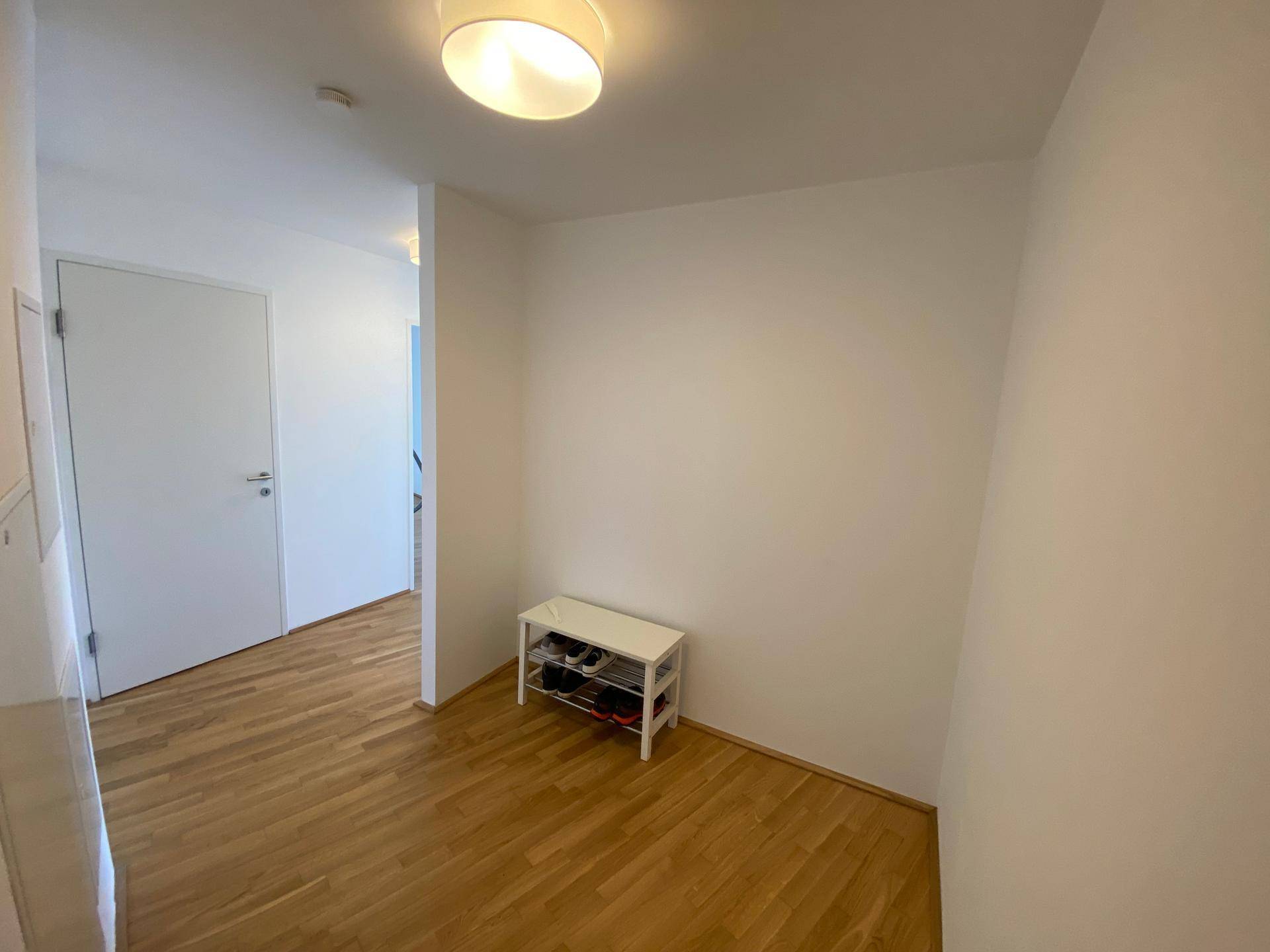 Eingangsbereich mit hellem Parkettboden und einer kleinen, praktischen Schuhablage.