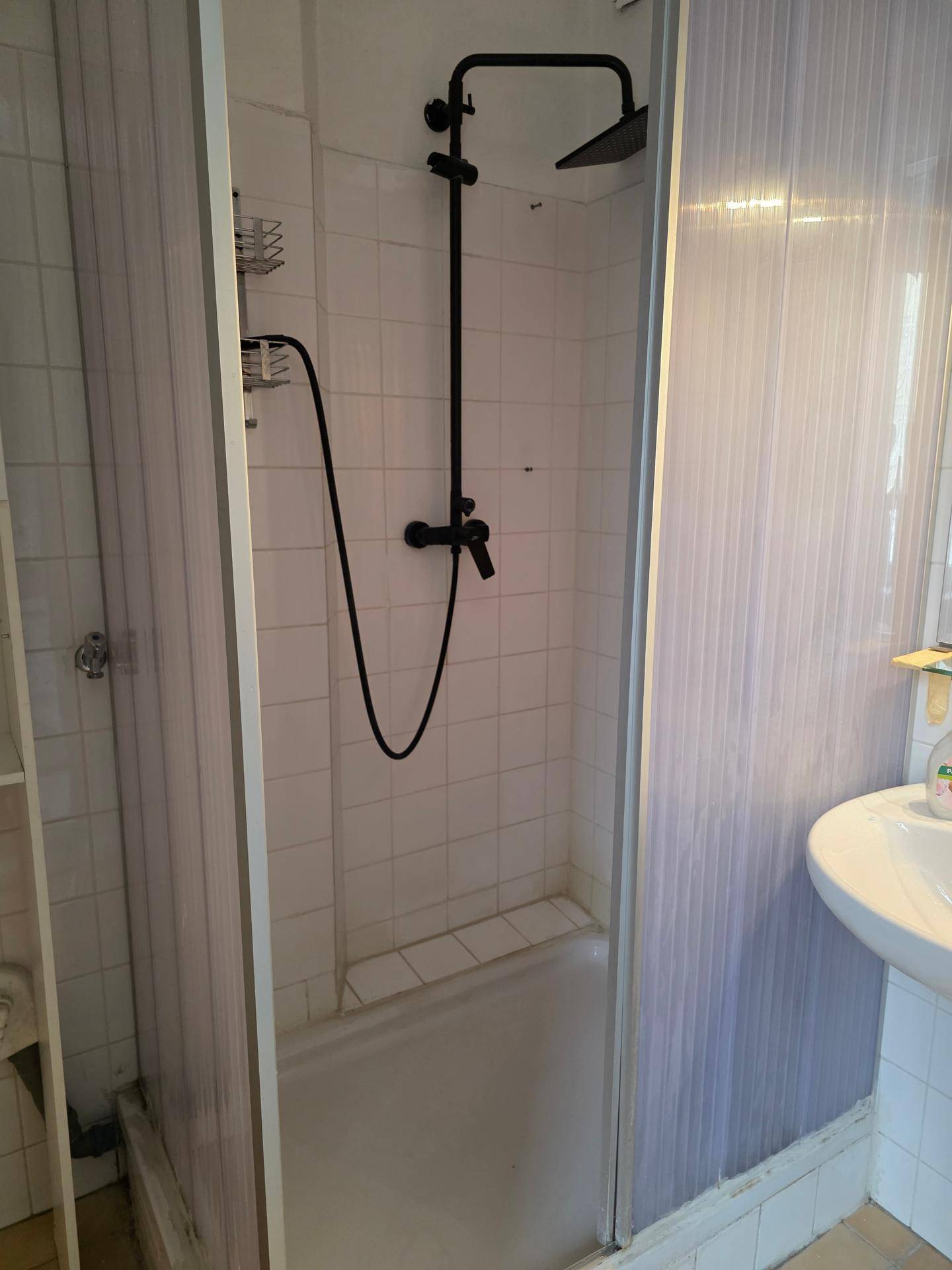 Badezimmer mit Duschkabine, weißen Fliesen und moderner schwarzer Regendusche.