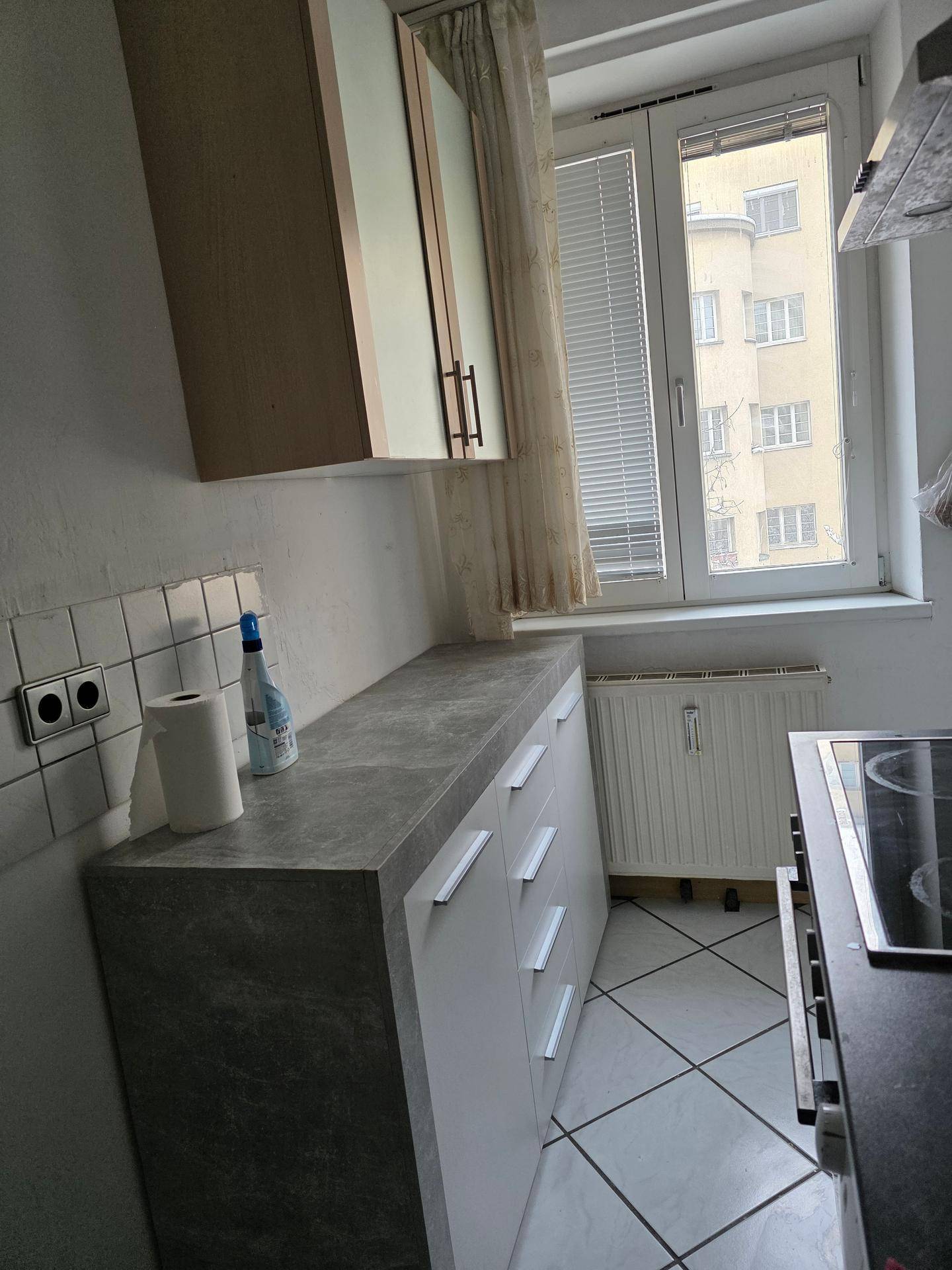 Küchenzeile mit dunkler Arbeitsplatte und weißen Unterschränken, mit Blick aus dem Fenster.