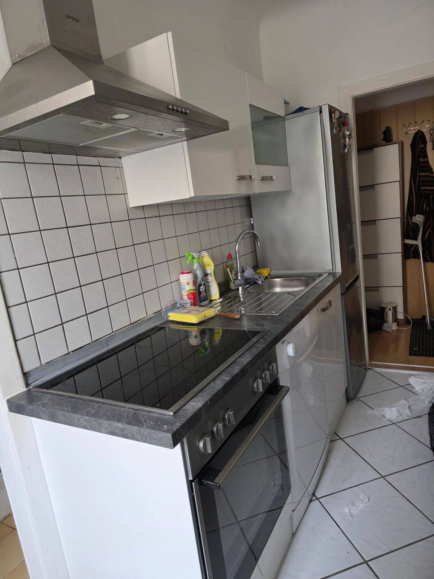 Funktionale Küche mit Spüle, Kühlschrank und weißen Wandfliesen, praktisch eingerichtet.