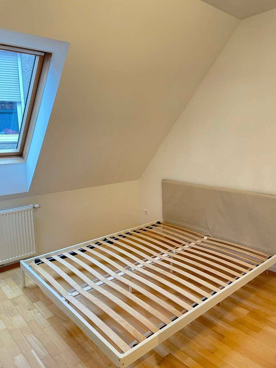Schlafzimmer mit Parkettboden, Dachfenster und einem Bettgestell unter der Dachschräge.