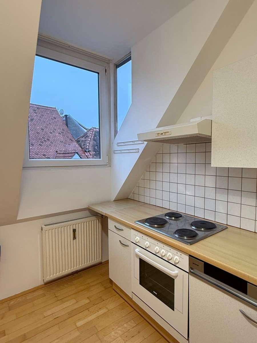 Kleine Küche im Dachgeschoss mit Holzarbeitsplatte, Elektroherd und Fenster mit Dachblick.