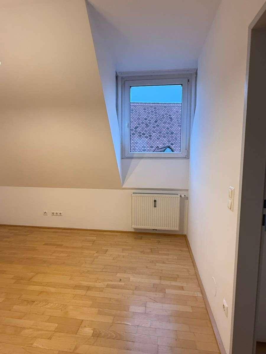Schlafzimmer mit Parkettboden, Fenster und Heizkörper unter der Dachschräge.