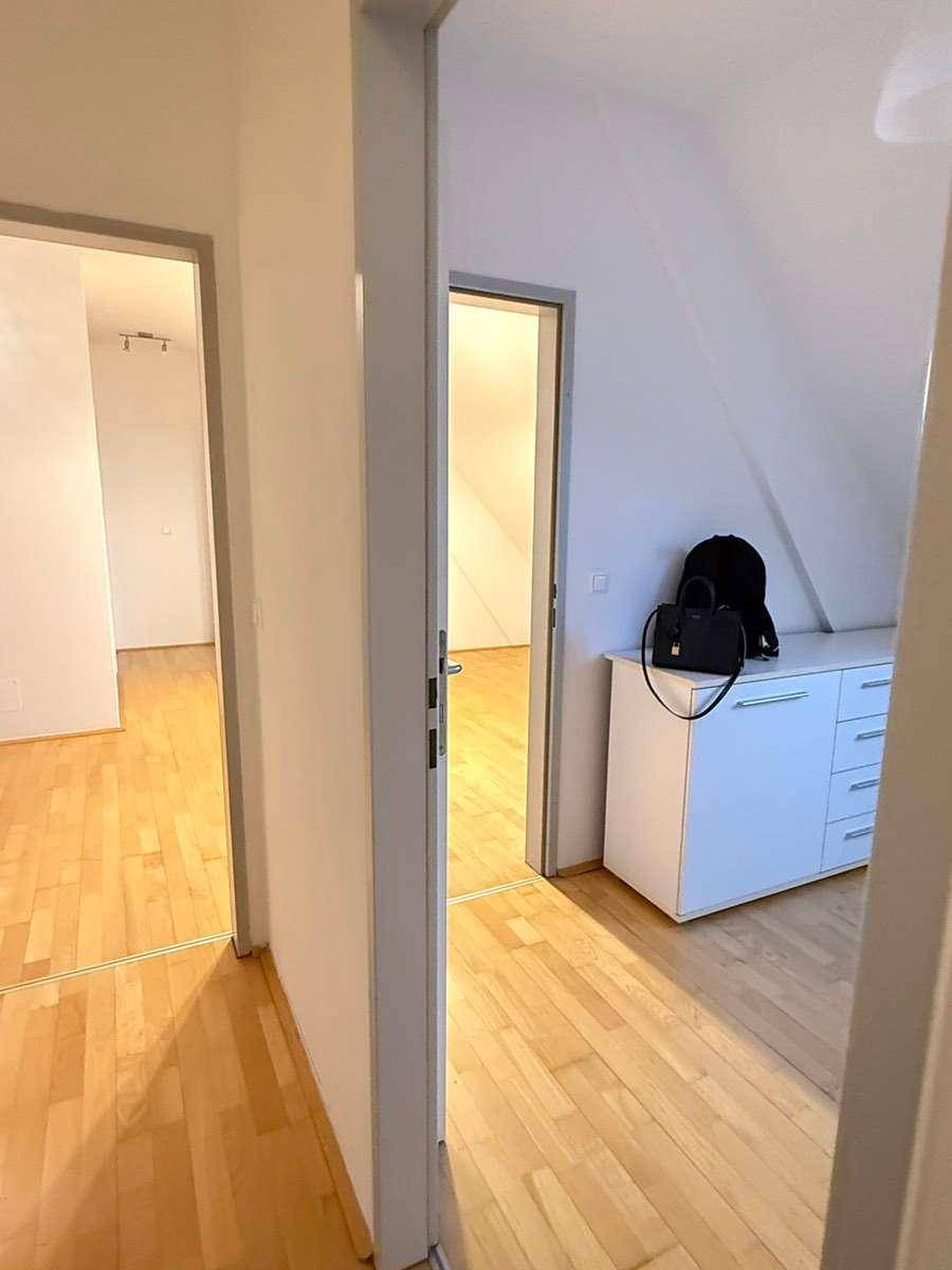 Flur mit Parkettboden und Zugang zu Zimmern im Dachgeschoss mit schrägen Wänden.