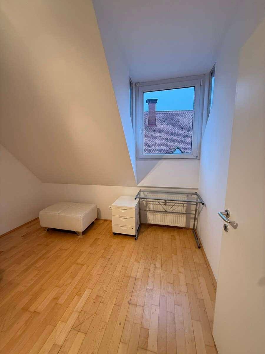 Schlafzimmer mit Parkettboden, Dachschräge und einem Fenster, das Tageslicht hereinlässt.
