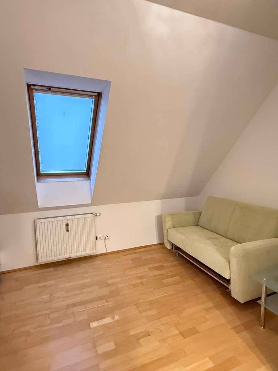 Heller Wohnraum mit Parkettboden, Dachfenster und einem Sofa unter schräger Decke.