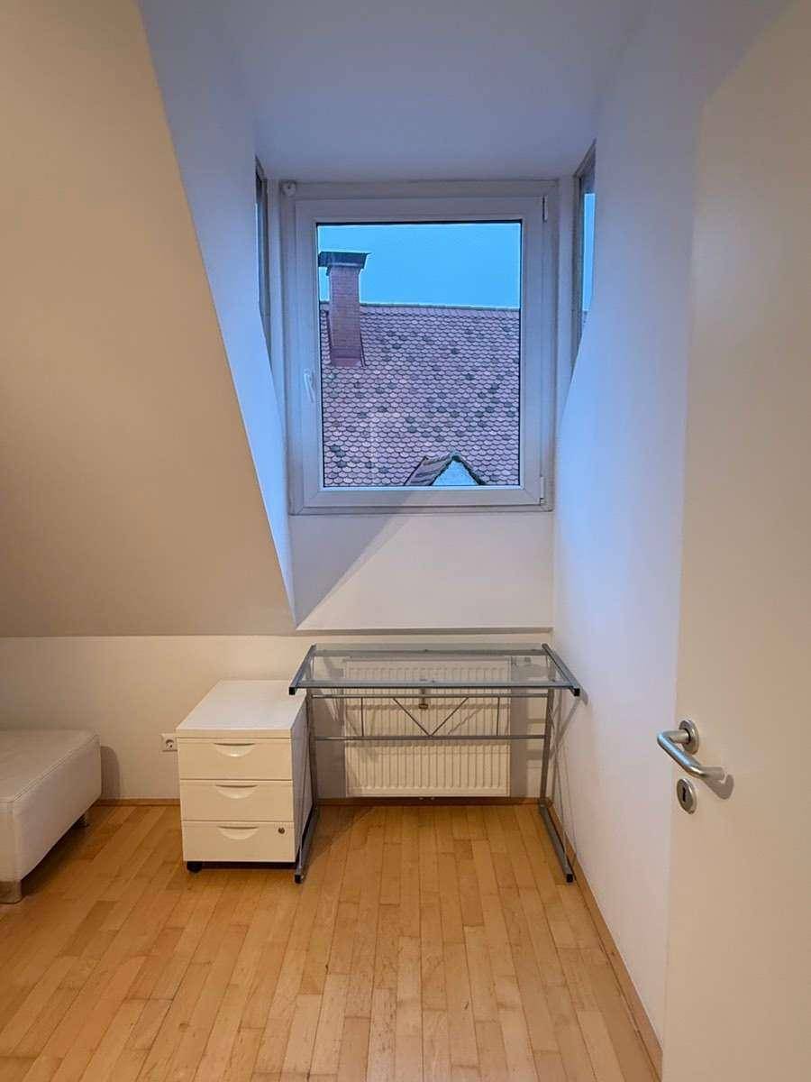 Schlafzimmer mit Parkettboden, Fenster und Schreibtisch unter der Dachschräge.