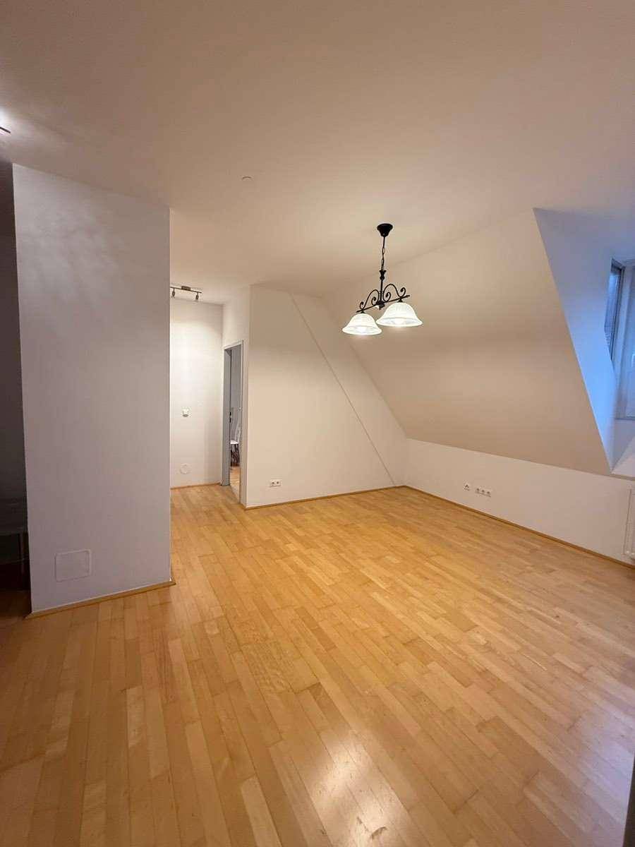 Geräumiges Wohnzimmer im Dachgeschoss mit Parkettboden, schrägen Wänden und Deckenleuchte.