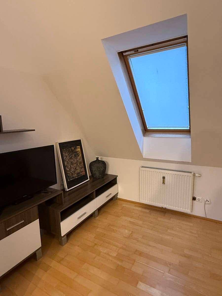 Wohnbereich mit Parkettboden, Dachfenster und Heizkörper, eingerichtet mit TV-Möbeln.