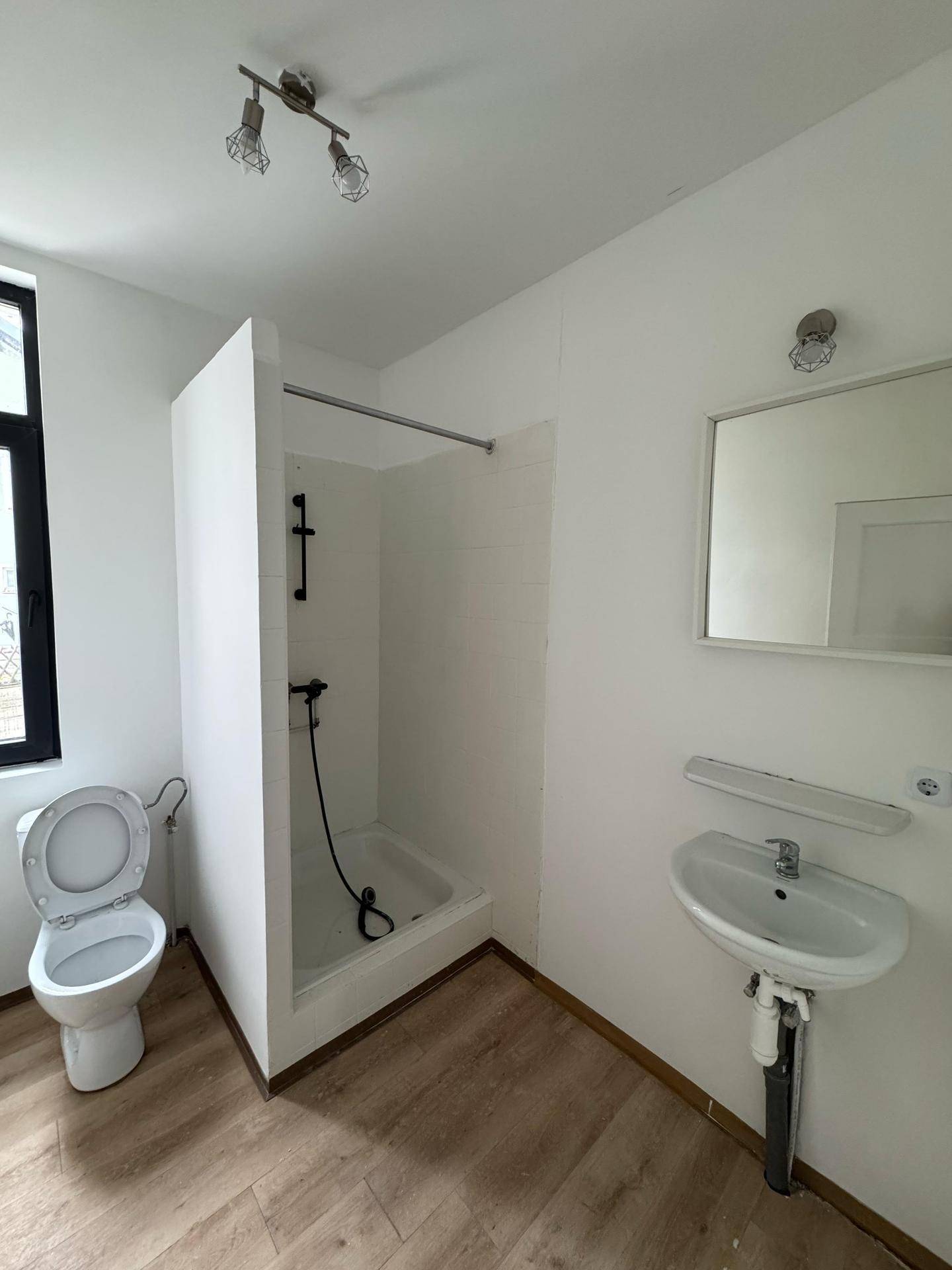 Einfaches Badezimmer mit Duschkabine, WC und Waschbecken in hellem Design.