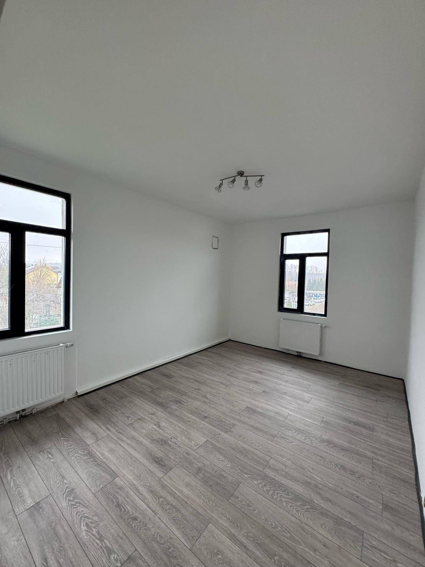 Geräumiger Raum mit Laminatboden, weißen Wänden und zwei Fenstern für viel Licht.
