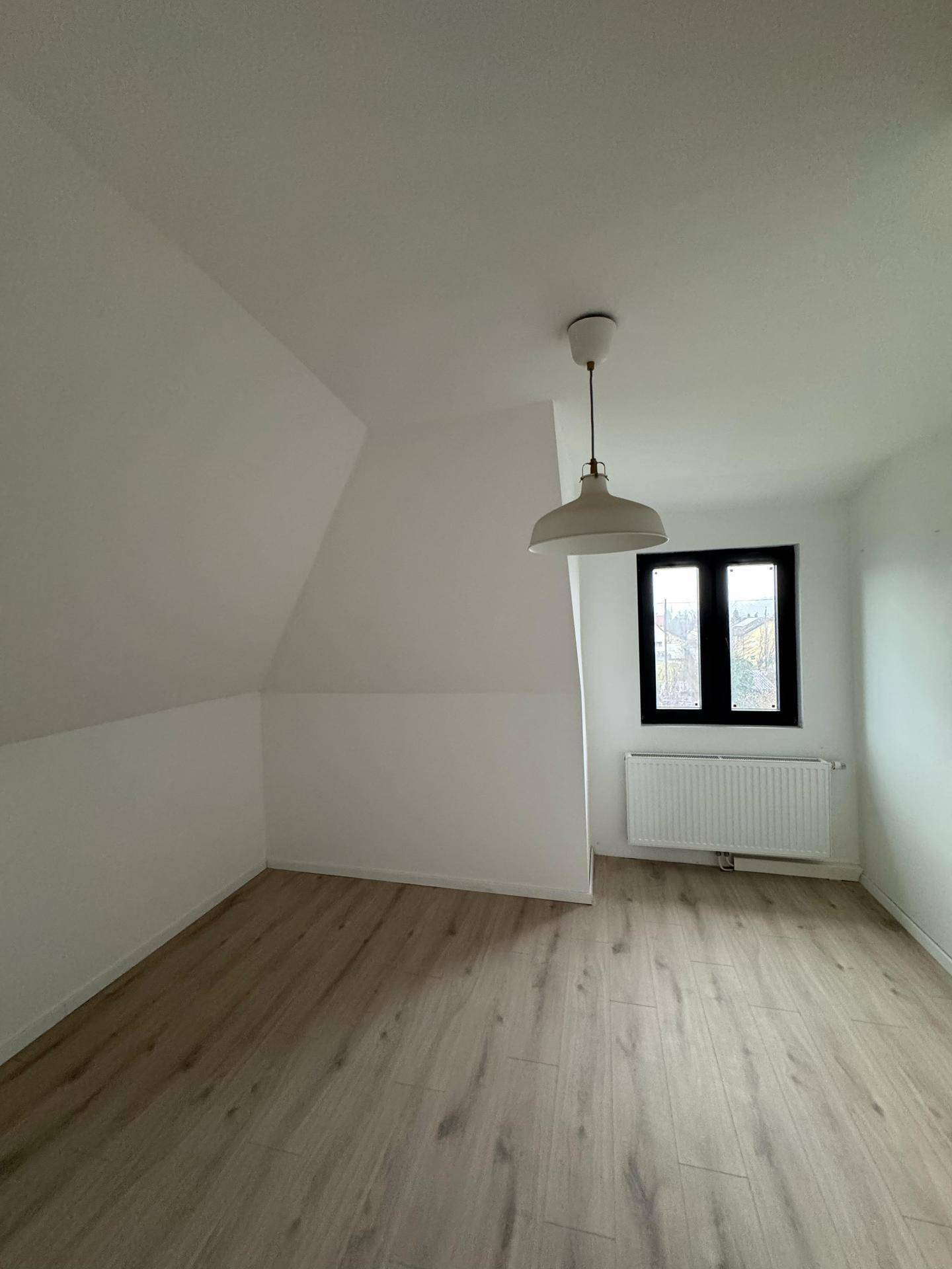 Dachgeschosszimmer mit Laminatboden, schrägen Wänden und Fenster mit Heizkörper.
